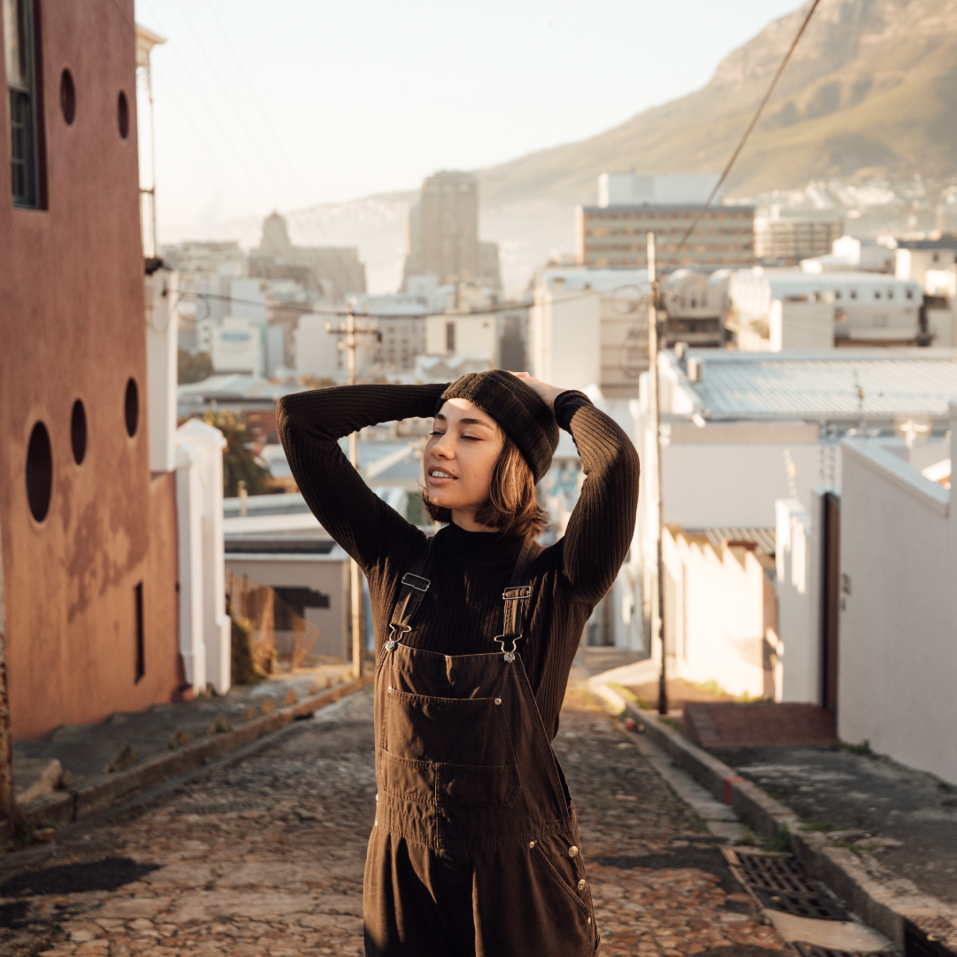 A woman stands in between buildings in the middle of a local road with her hands on her head