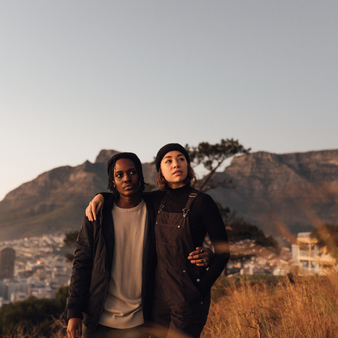 A man and a woman with their arms around each other stand in a grassy field in Cape Town