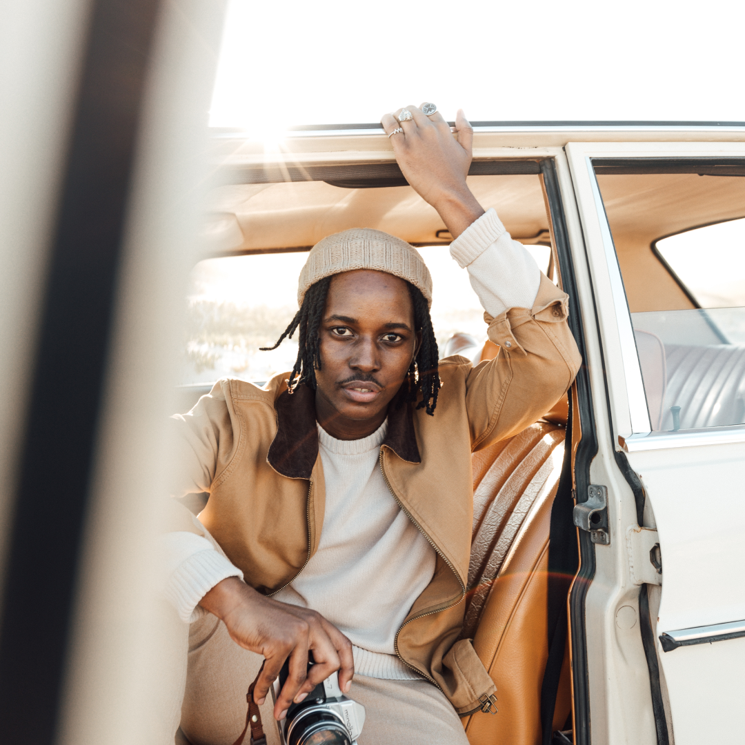 A man sitting inside a car with the door open, holding a camera