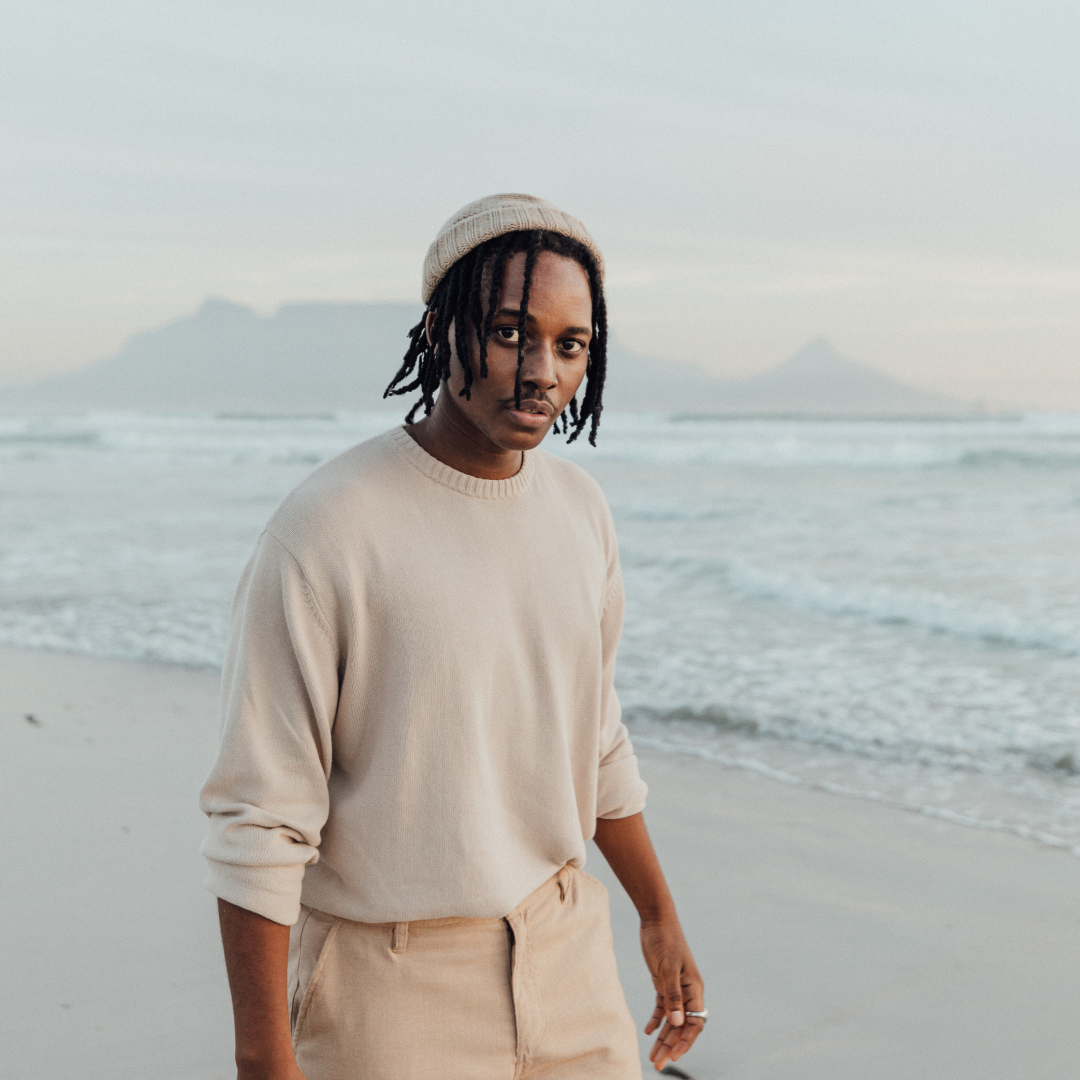 A man wearing a wool beanie is walking along the beach shore