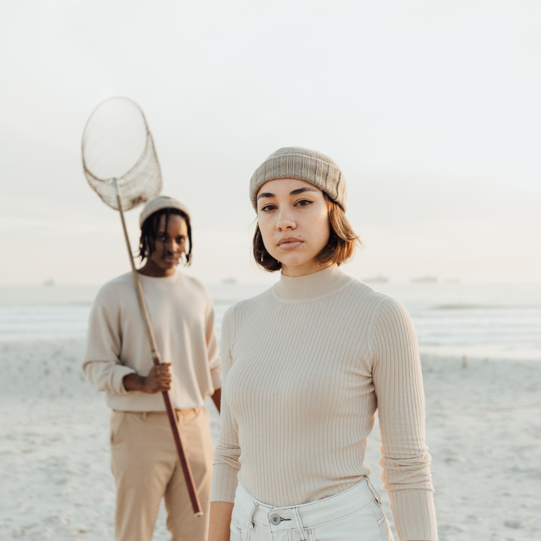 A woman and a man standing on the beach, the man is holding a fishing net