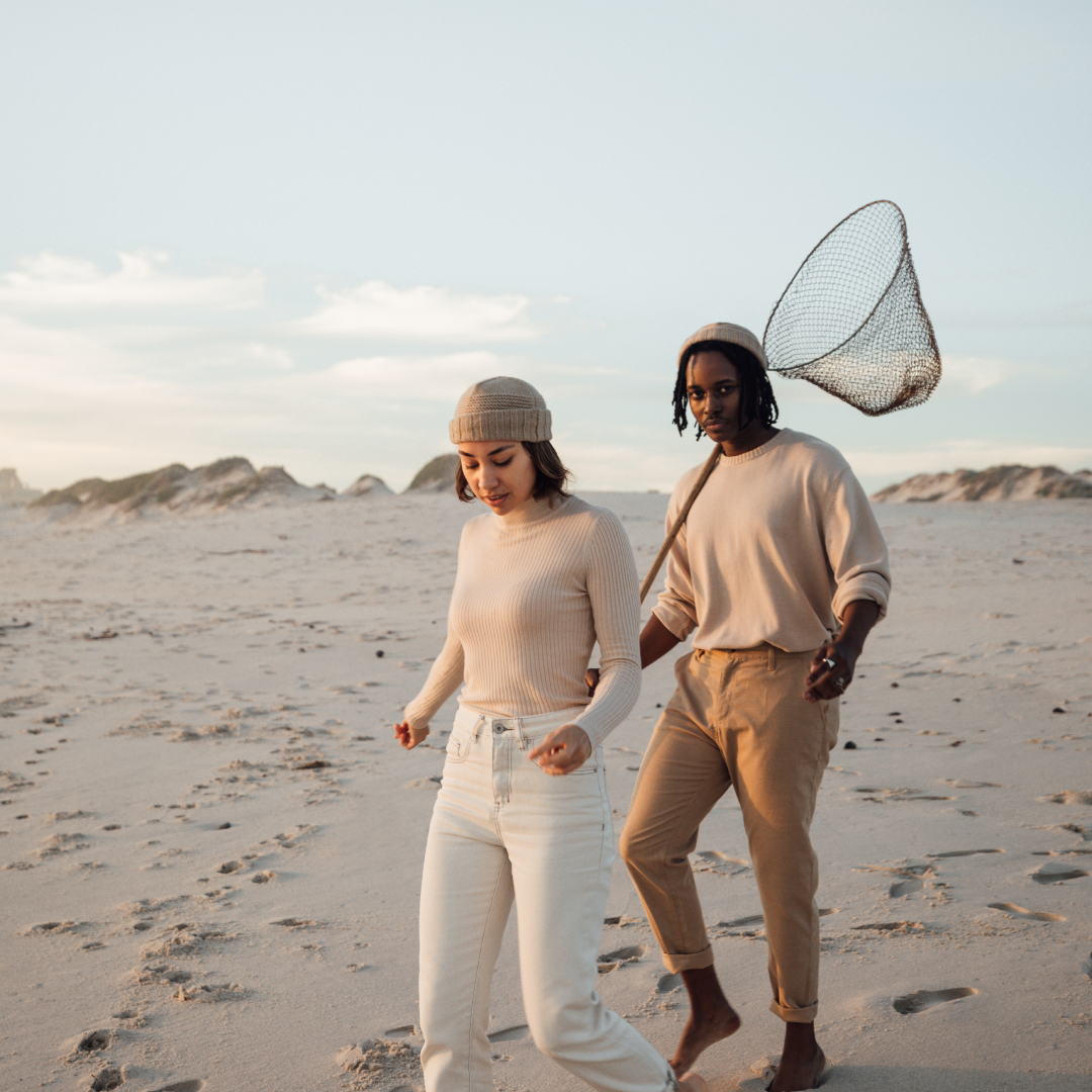 A man and woman running along the beach, the man is holding a fishing net