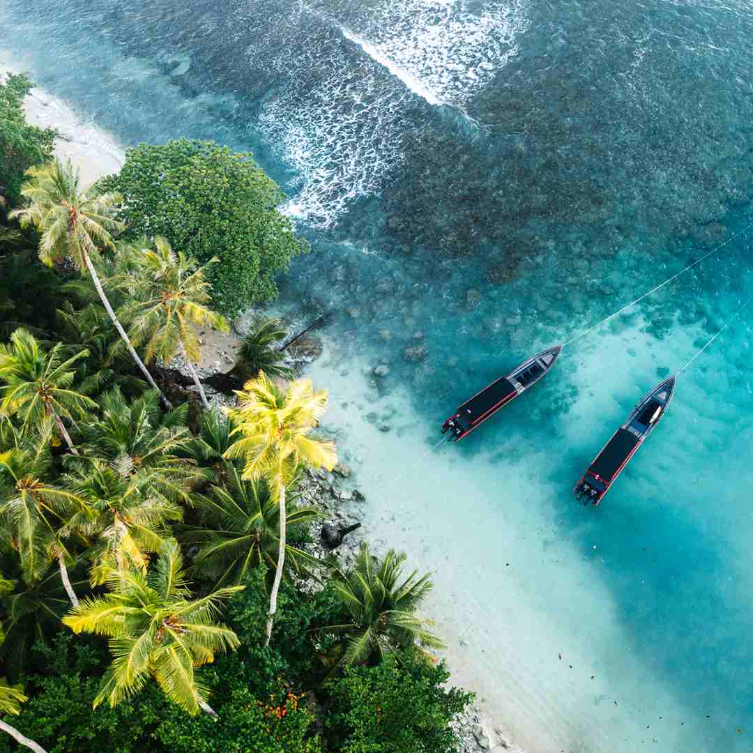 Aerial photo of two boats anchored near the shore of an island full of palm trees