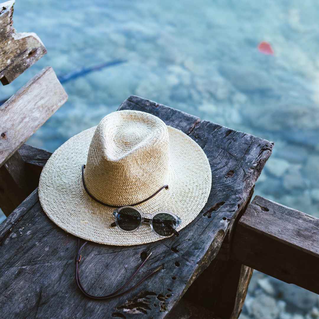 Marc's Rider Bone straw hat sits on a wooden board with his sunglasses resting on top