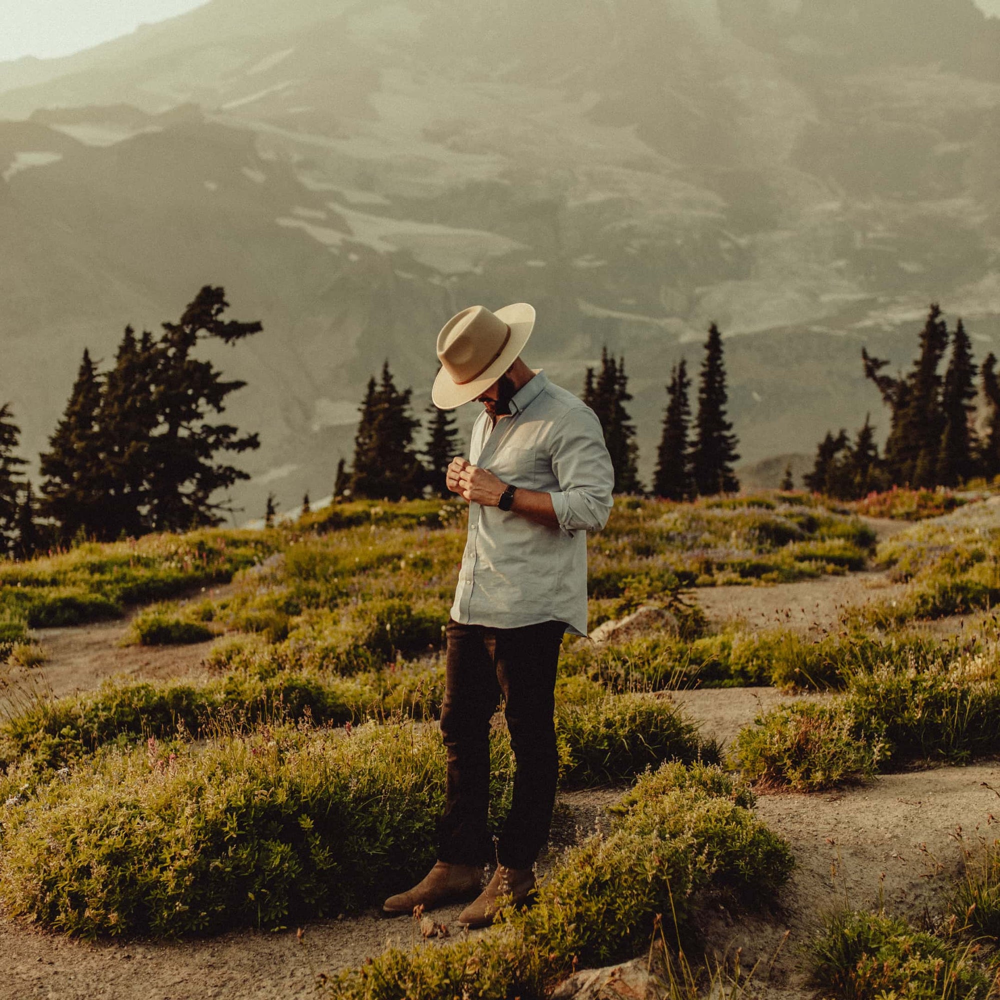 A man is standing in a wild flower field amongst the mountains