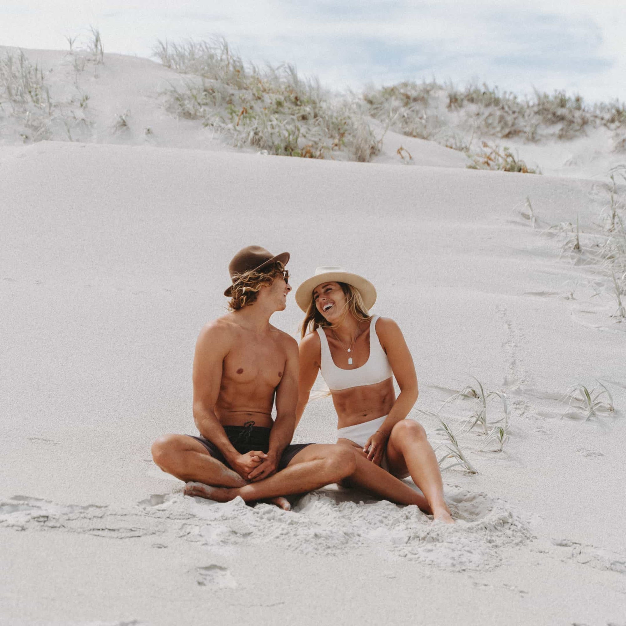 Glen and Kendall sitting next to each other on the beach, laughing