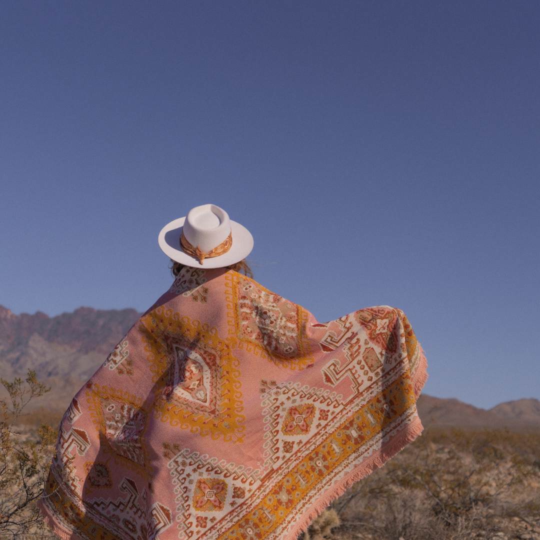 Sharnee in the desert with her hat on and wrapped in a wandering folk throw