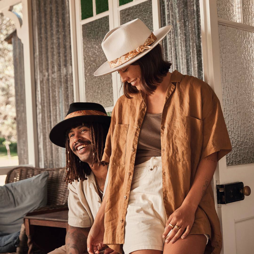 A man and a woman standing at the front of a cabin wearing hats