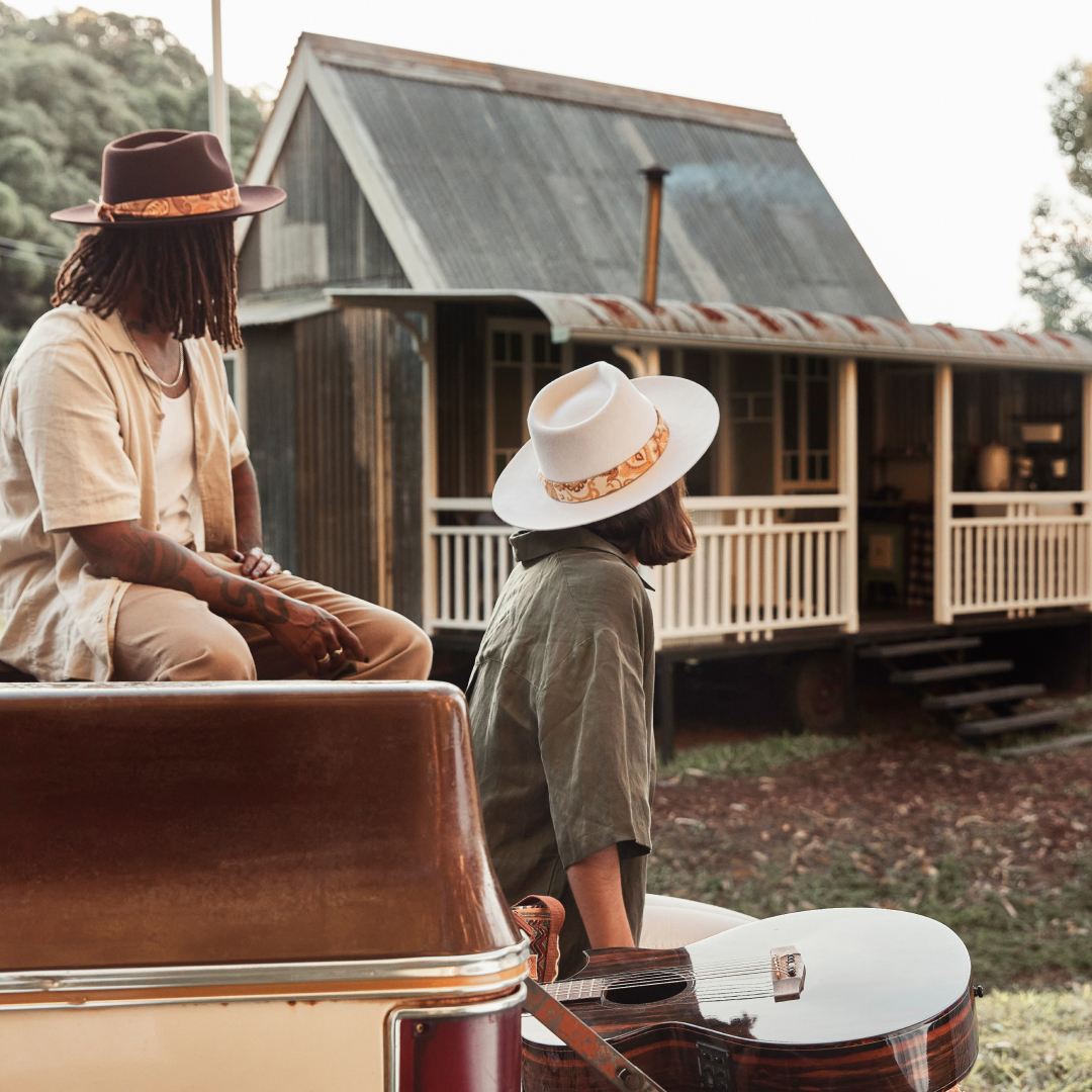 Young couple sitting on the back of a small truck looking at a cabin in the background