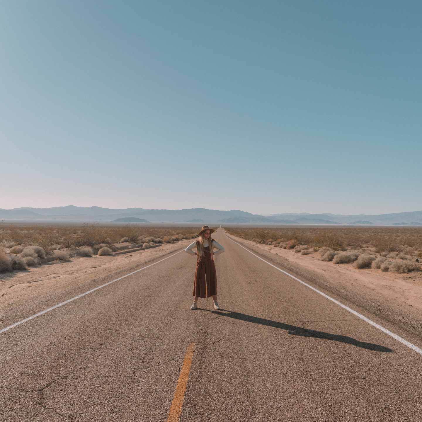 Sharnee standing in the middle of an open desert road and mountains in the background