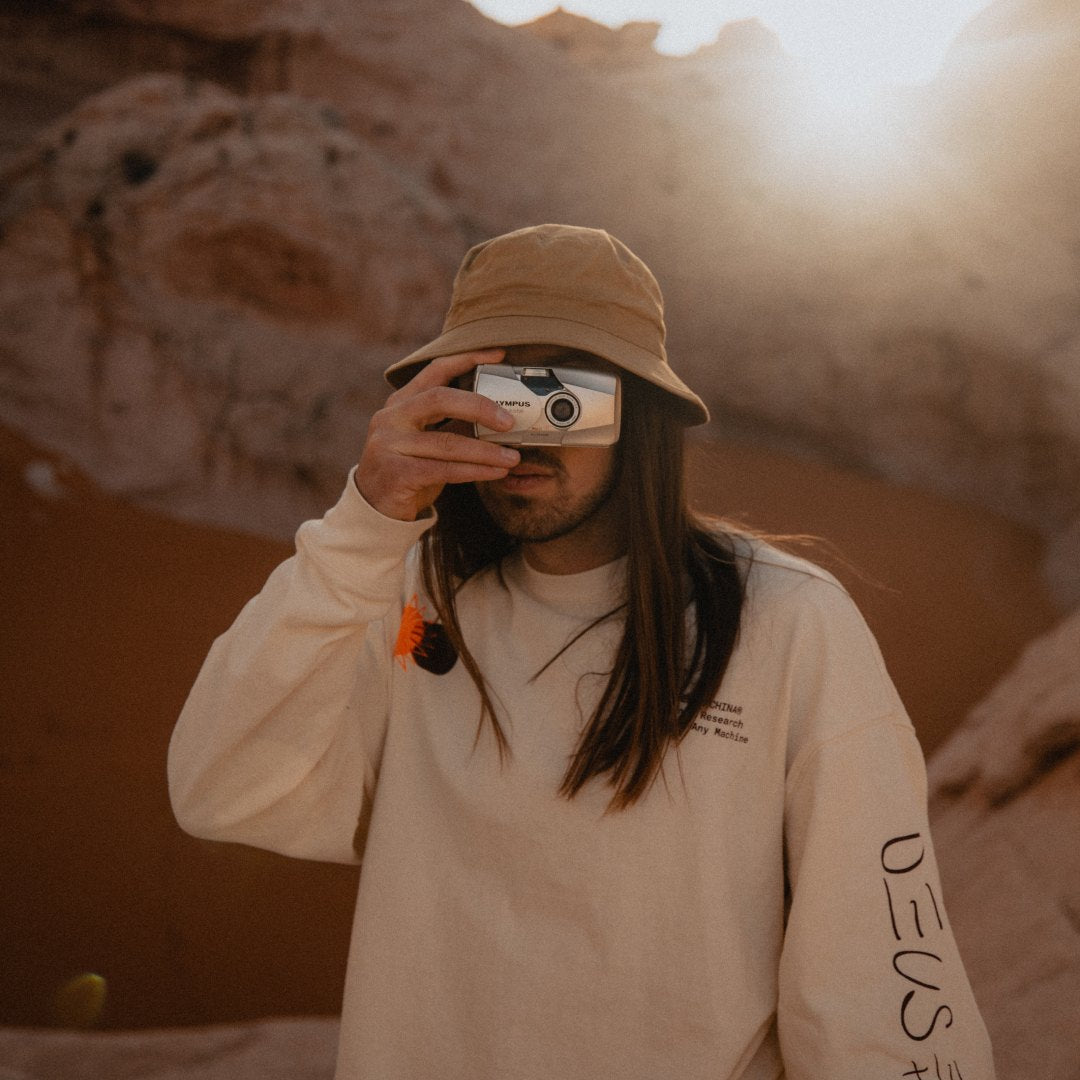 A man with long brown hair wearing a bucket hat taking photos on a film camera