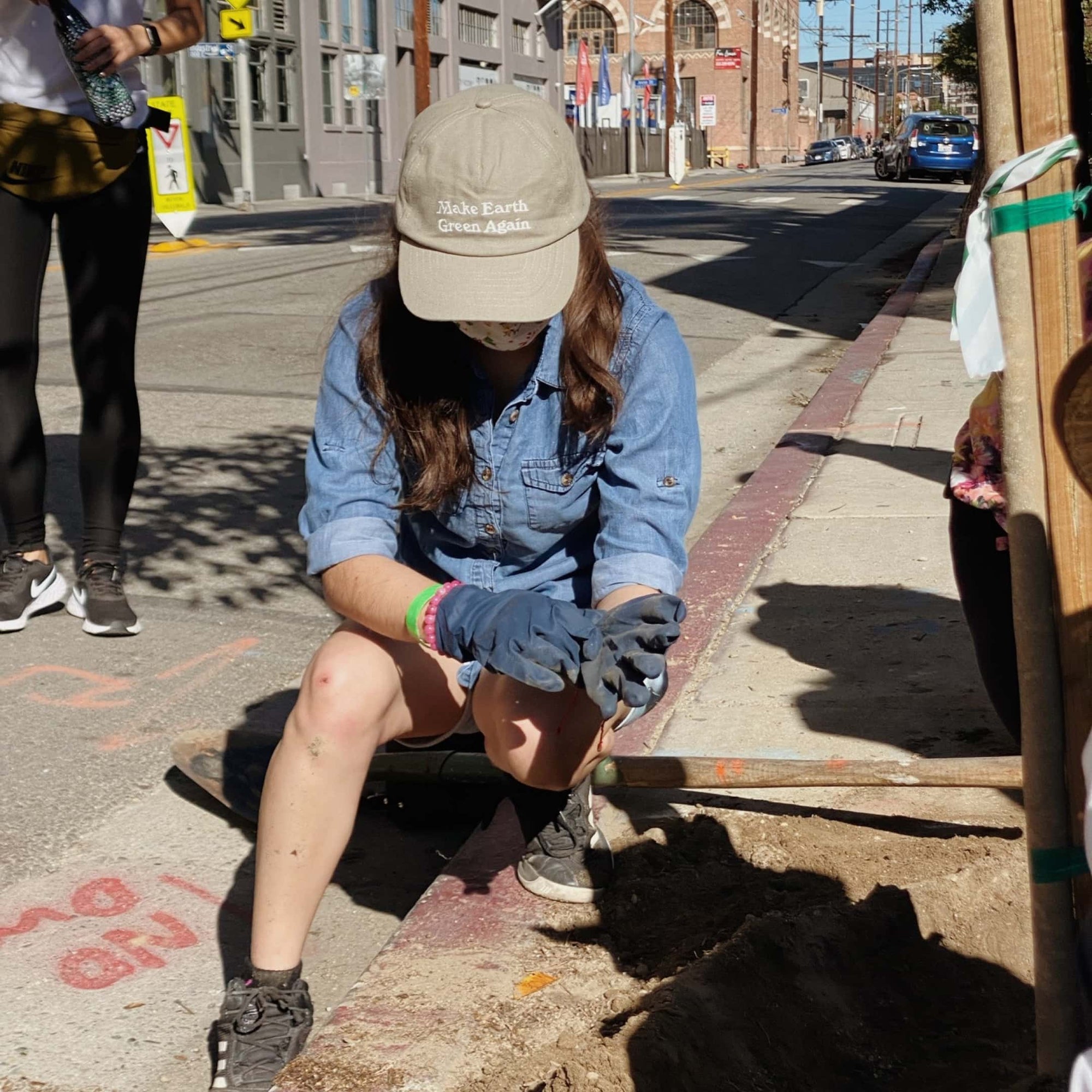 A woman is kneeling down to pull her gardening gloves on