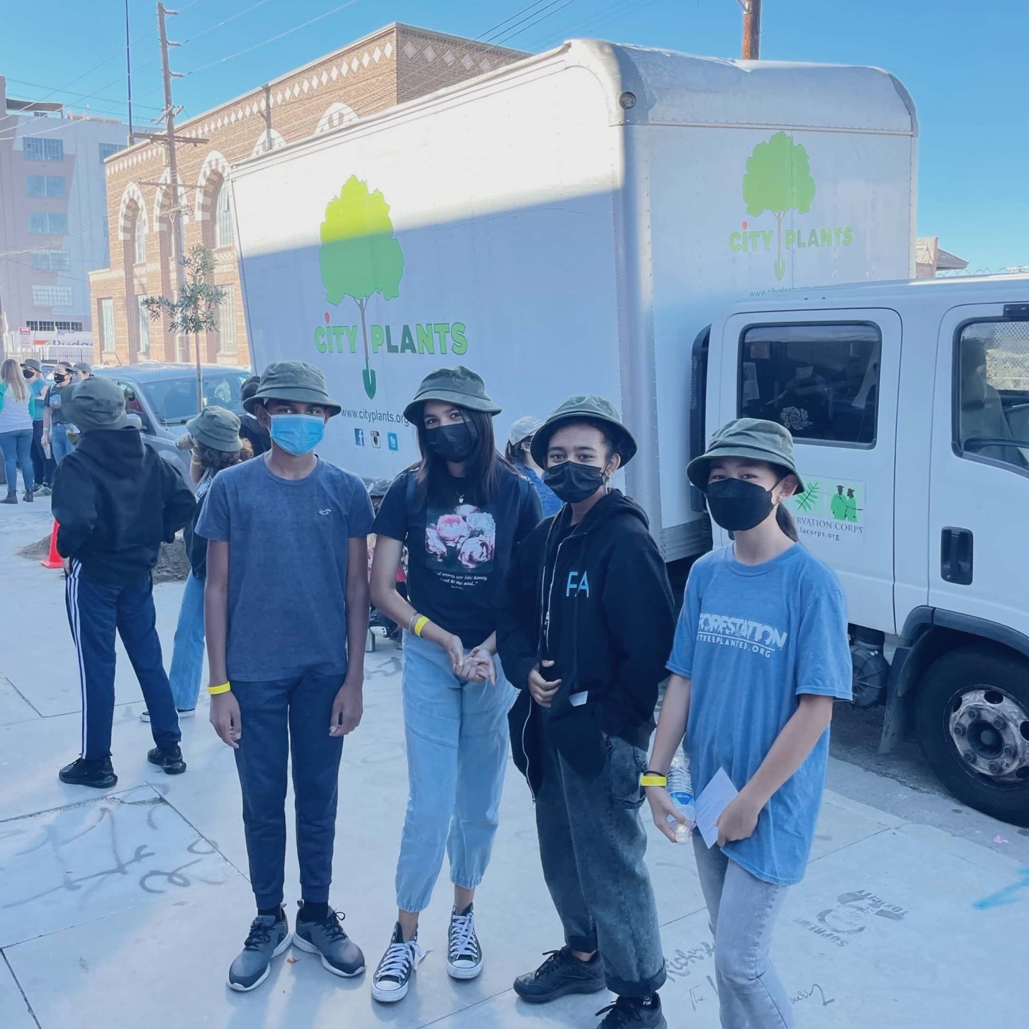 Four young people are standing together wearing masks and bucket hats looking at the camera