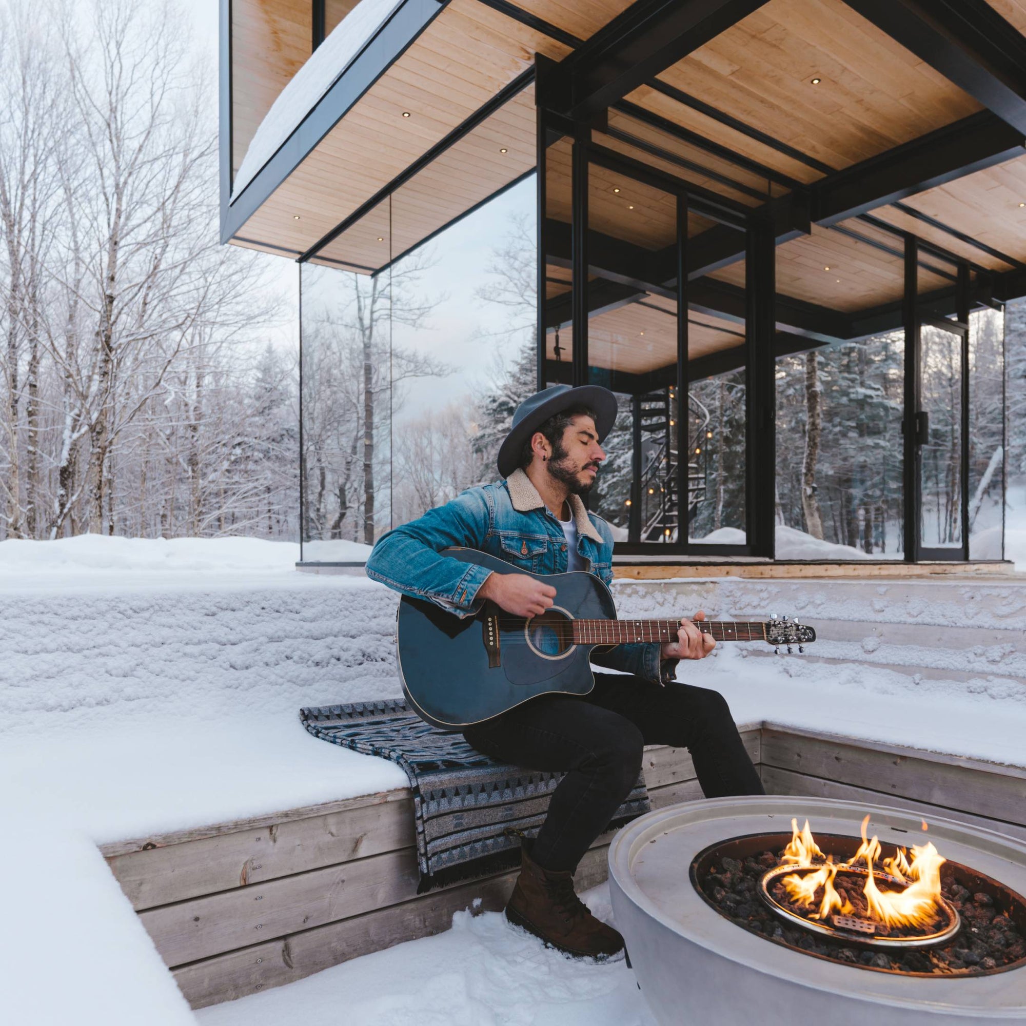 Jenna's partner sits by the outdoor fire pit in the snow while playing his guitar