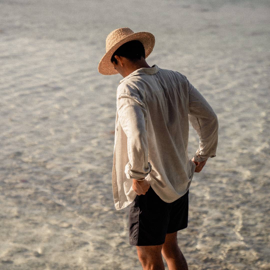A man with short black hair wearing a wide brim straw hat is looking down at the ocean.