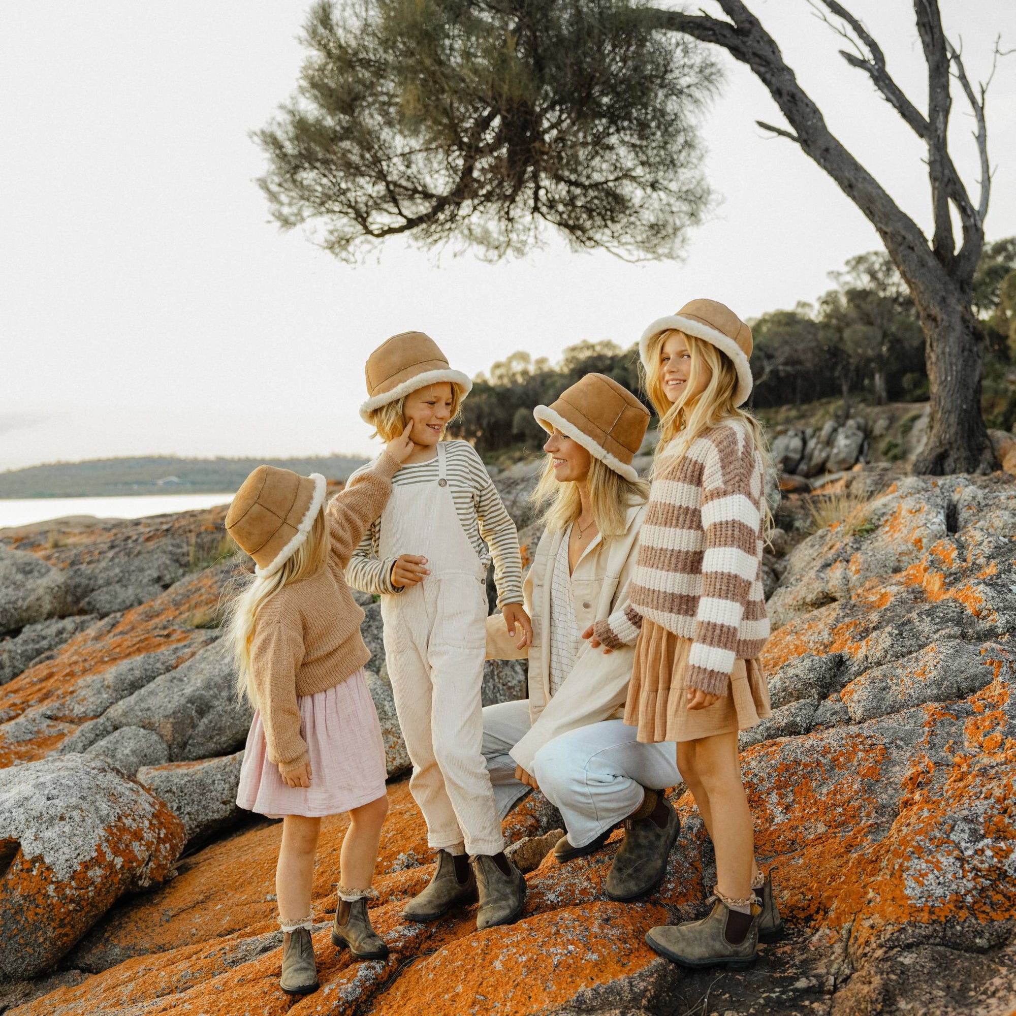 A mother and her three children all standing on rocks by the ocean in Tasmania wearing ugg bucket hats
