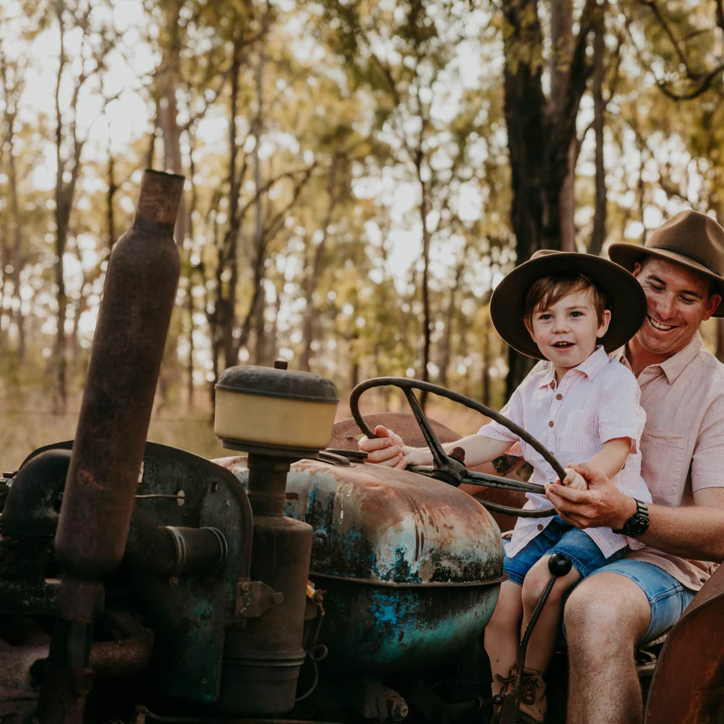 A man and his son sit on a tractor wearing matching hats