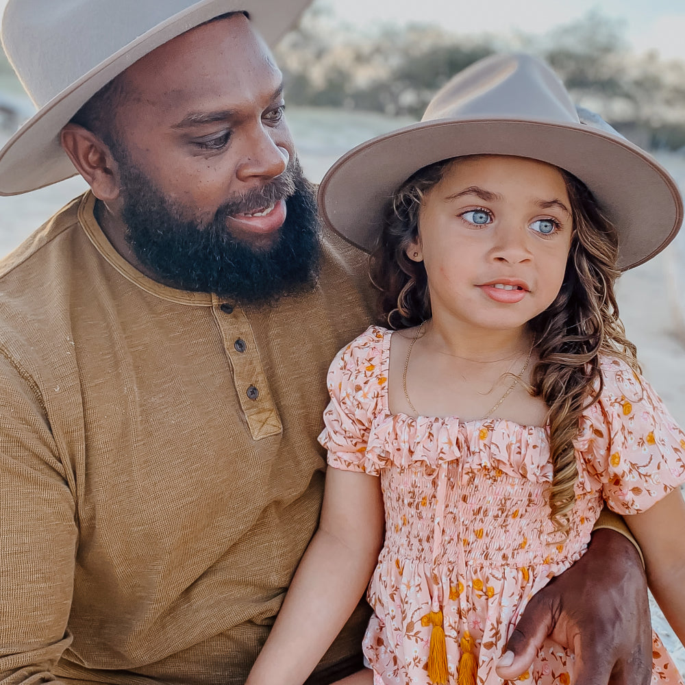 A man holding his daughter, they are both wearing matching wide brim wool hats