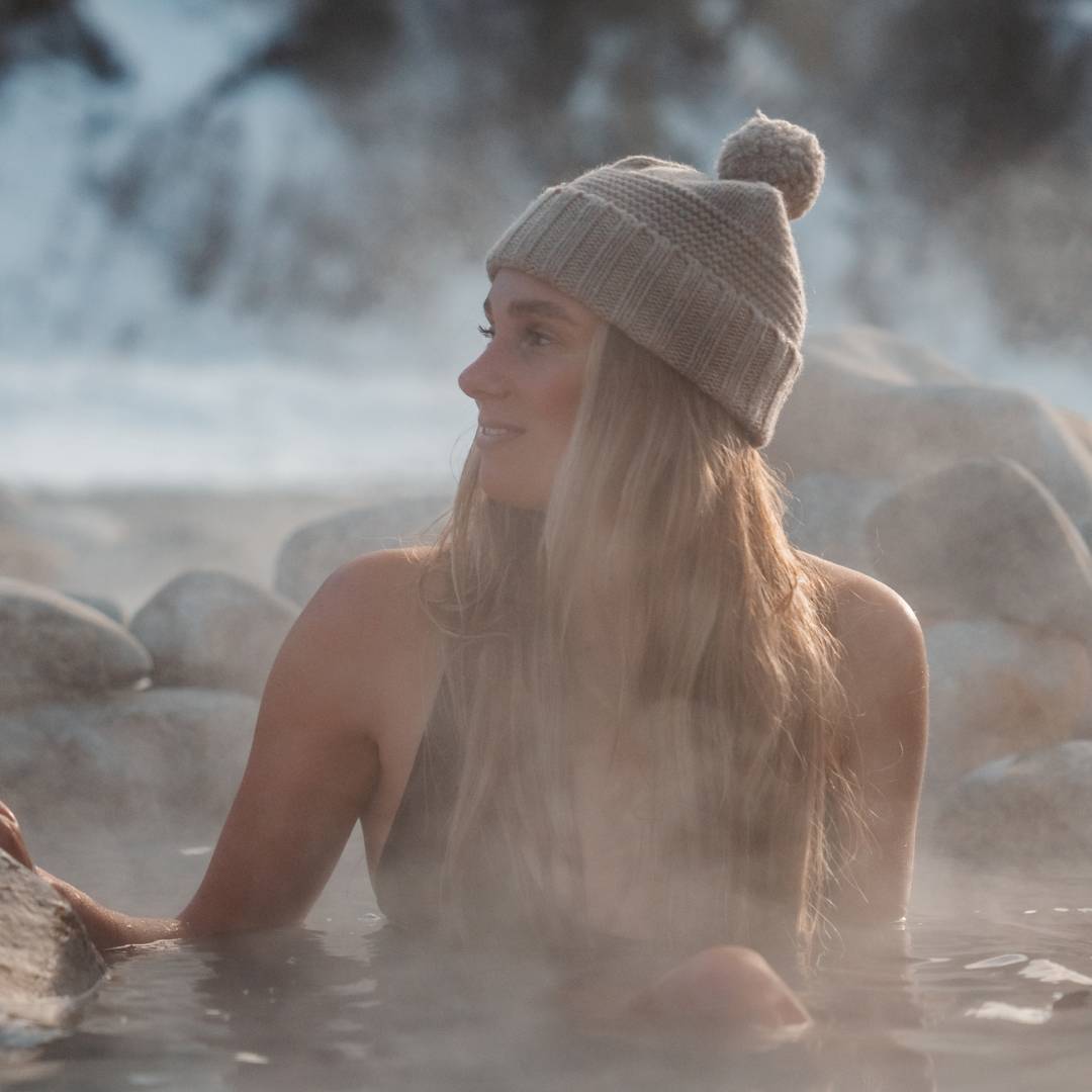 Woman with long hair wearing a beanie, sitting in a hot spring