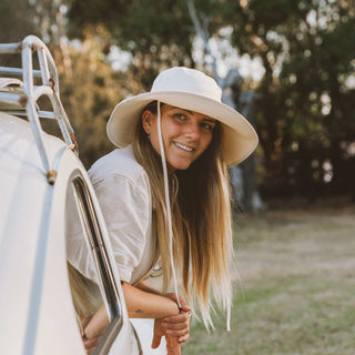 Woman riding in a car wearing the white cream bucket hat