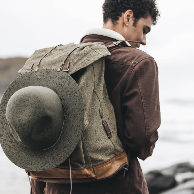 A man is walking with a backpack on and a wide brim hat strapped to the back of his bag