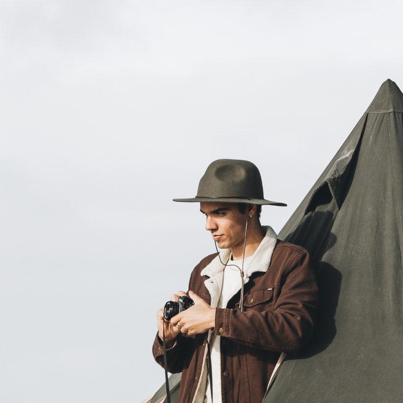 A man with short hair wearing a wide brim wool hat holding a film camera