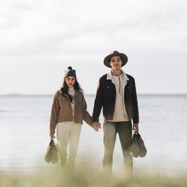 A woman and a man holding hands standing on the sand at the beach