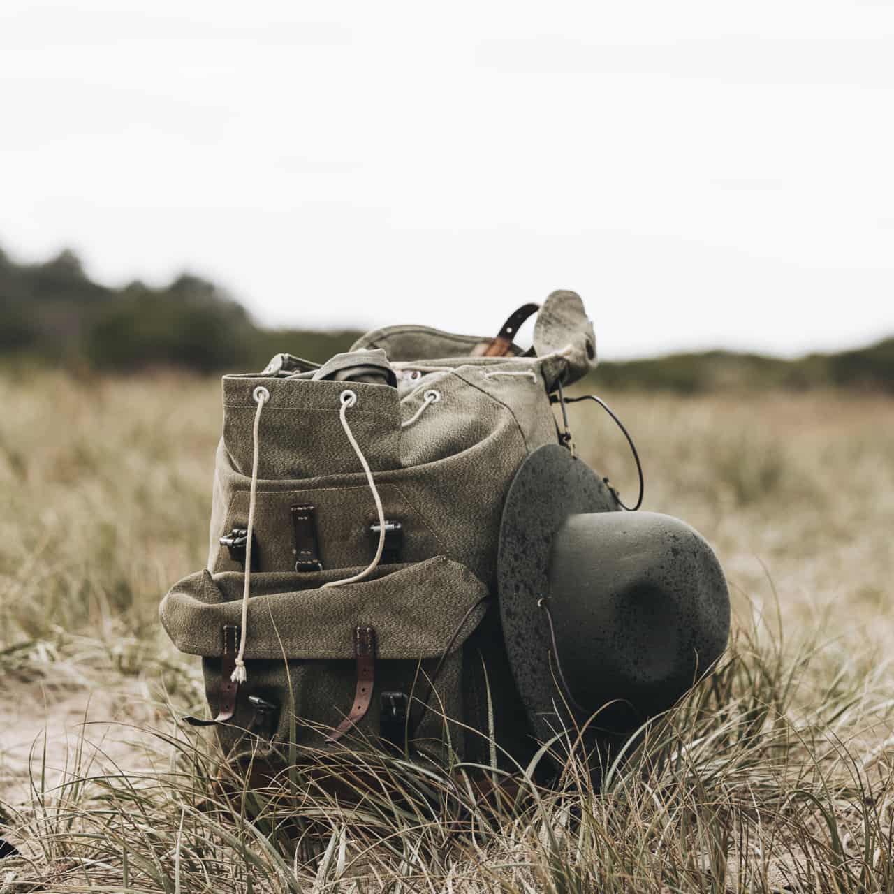 A wide brim wool hat attached to the side of a vintage hiking bag with hat clips